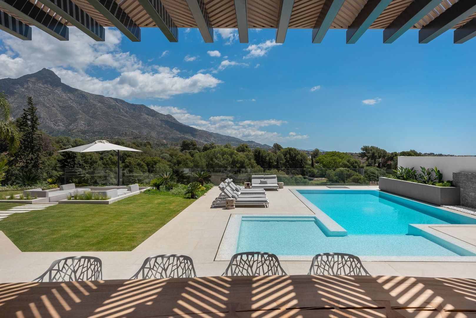 Panoramic pool terrace of Villa Aquila with pergola framing, mountain backdrop and open Mediterranean views
