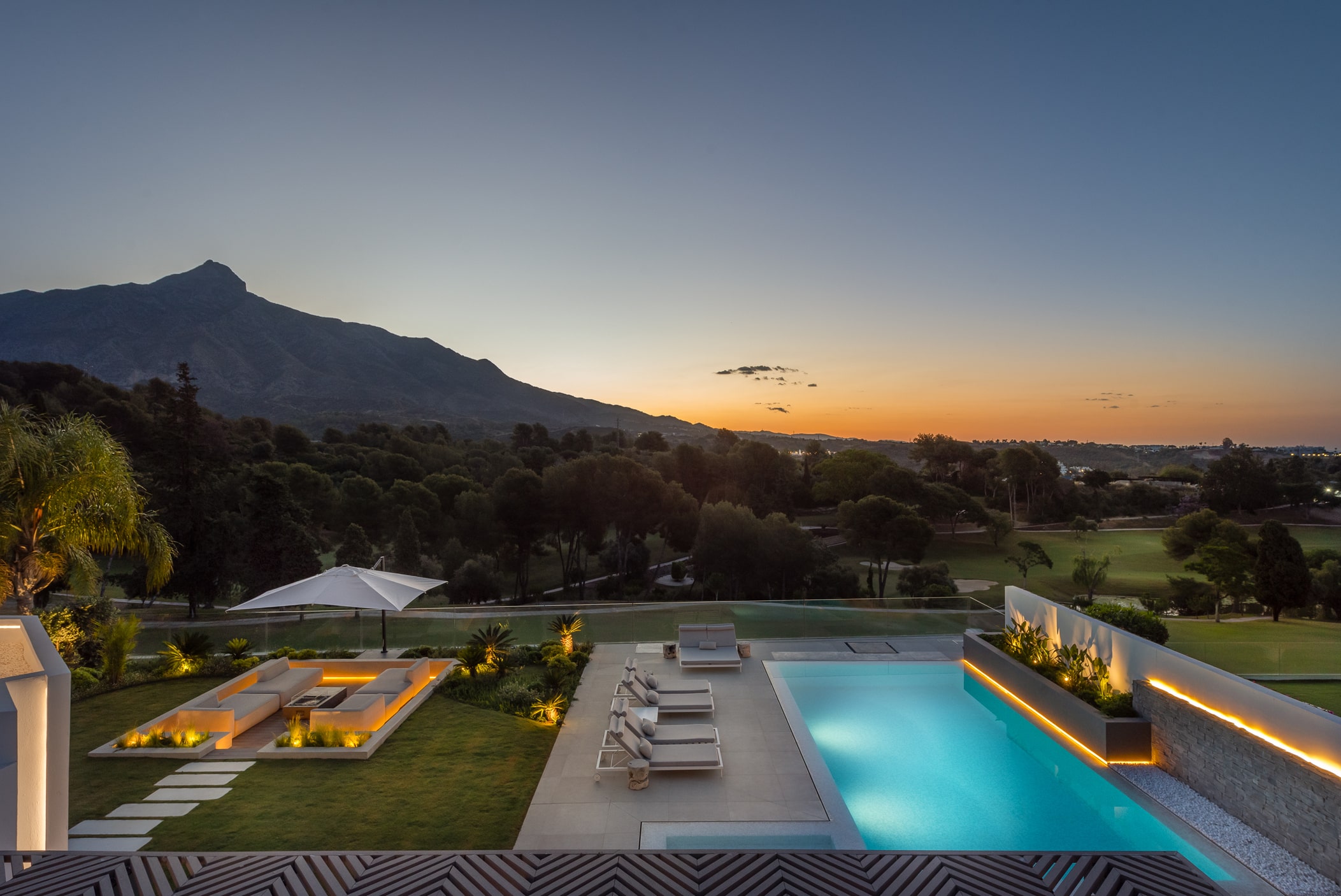 Sunset panoramic exterior of Villa Aquila with illuminated pool, lawn and distant mountain horizon in Marbella