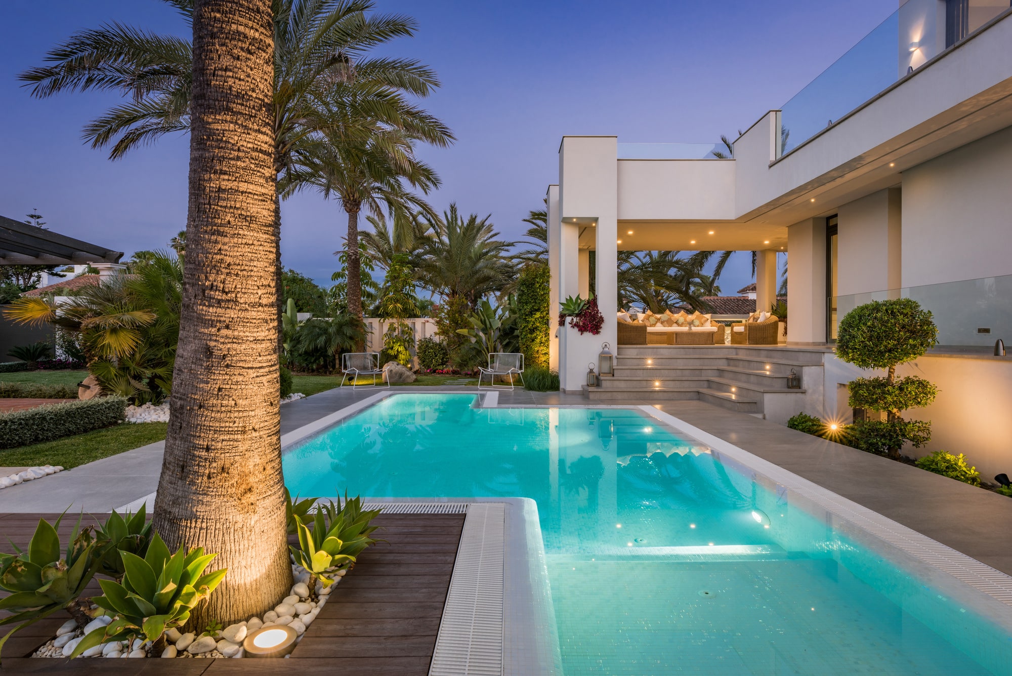 Twilight poolside view of Villa Australia with palm tree foreground, illuminated water and warm terrace lighting
