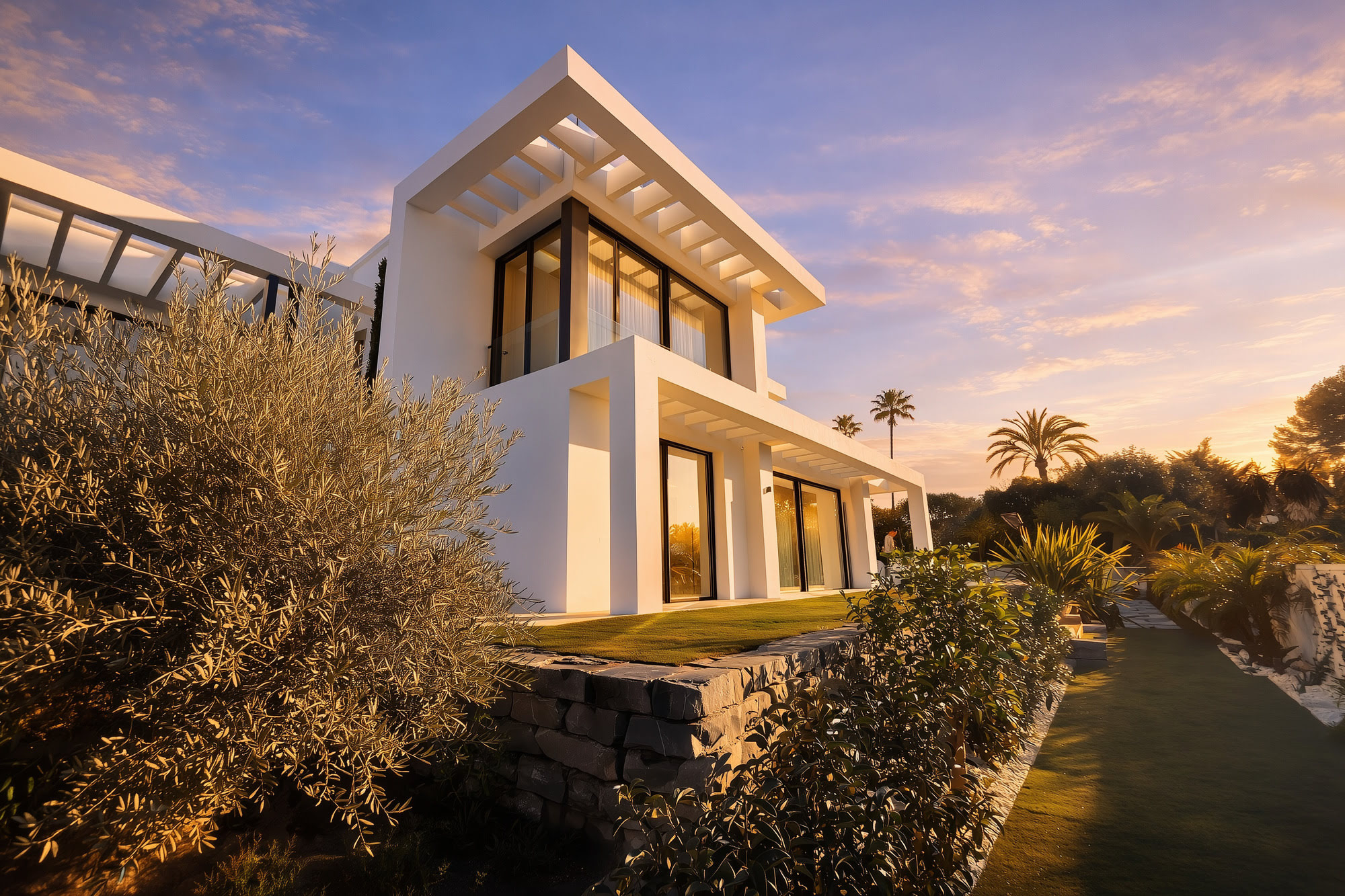 Low-angle exterior view of Villa Inés showing pergola lines, white volumes and planted rock garden