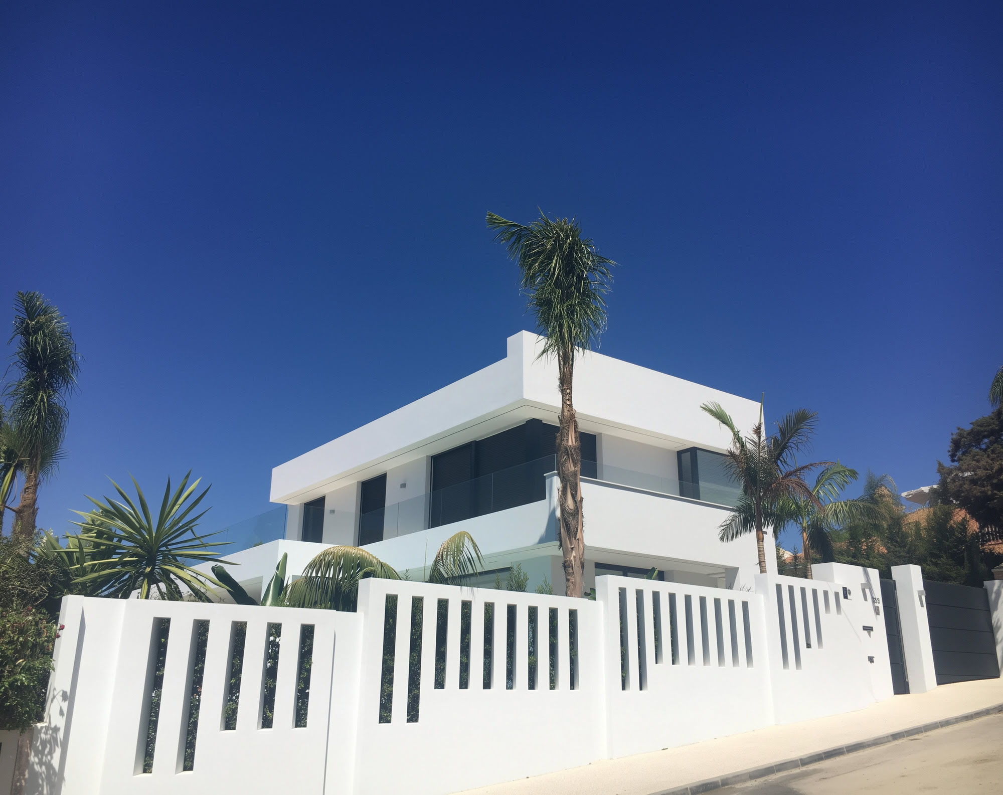 M152 front façade in Marbella East with sculptural white volumes, palm trees and minimalist entrance composition