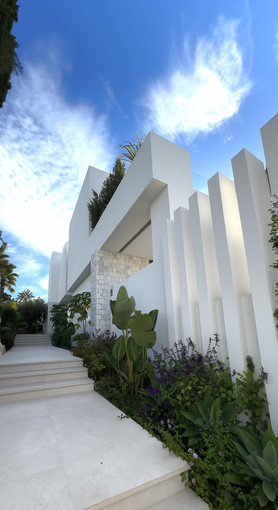 Sculptural side façade of M94 with vertical fins, textured white surfaces and planted approach