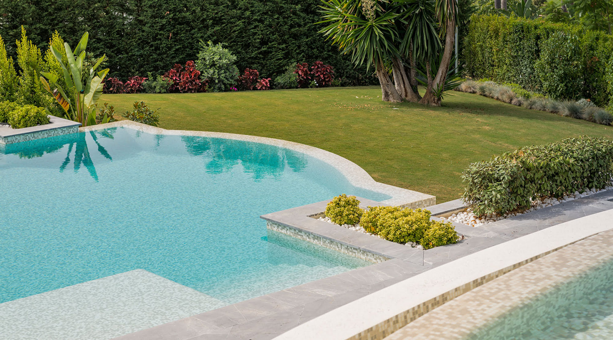 Curved swimming pool and lawn garden beside Villa Mariselena, showing refined outdoor living and lush landscaping