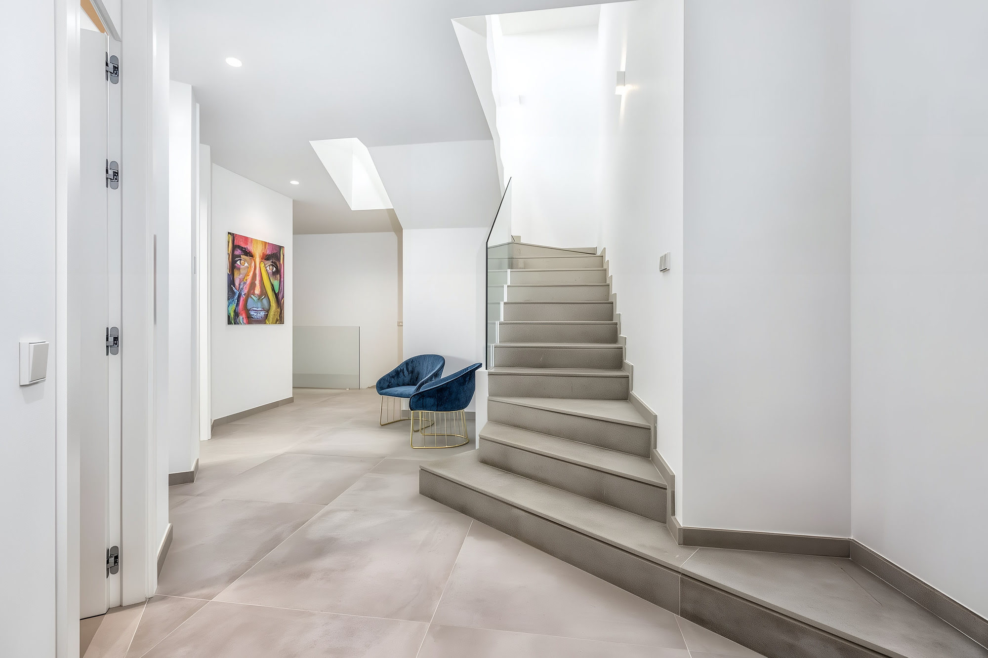 Interior circulation space at Villa Origami with staircase, white walls and continuous stone flooring