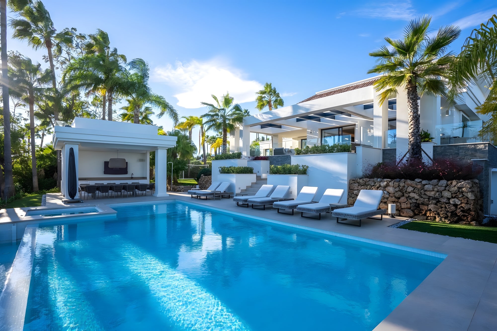 Daylight view of the swimming pool and main façade of Casa de las Palmeras framed by palms and Mediterranean planting
