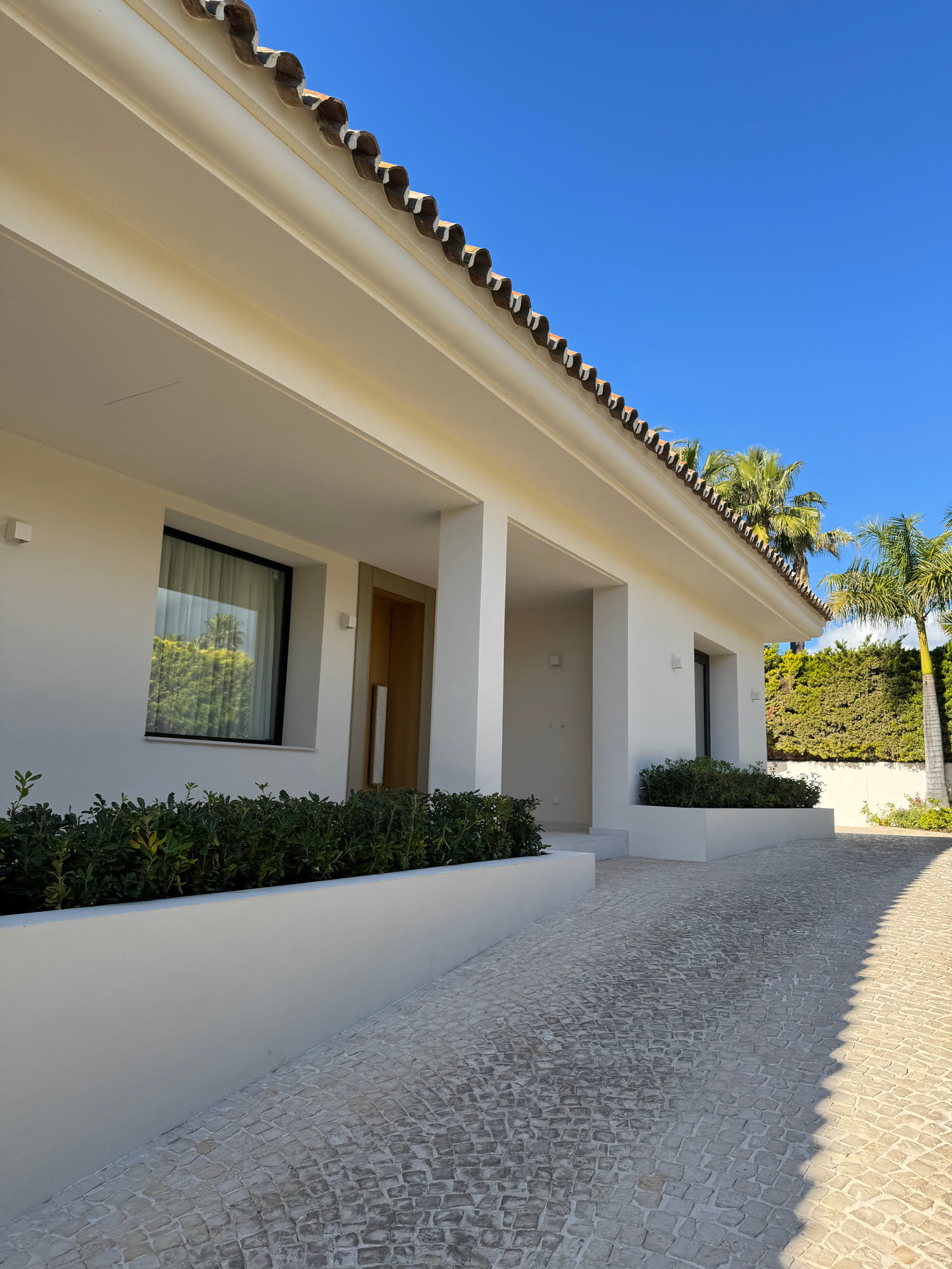 Columned exterior walkway and sheltered porch of Villa Shangri-La with warm white render and gravel path
