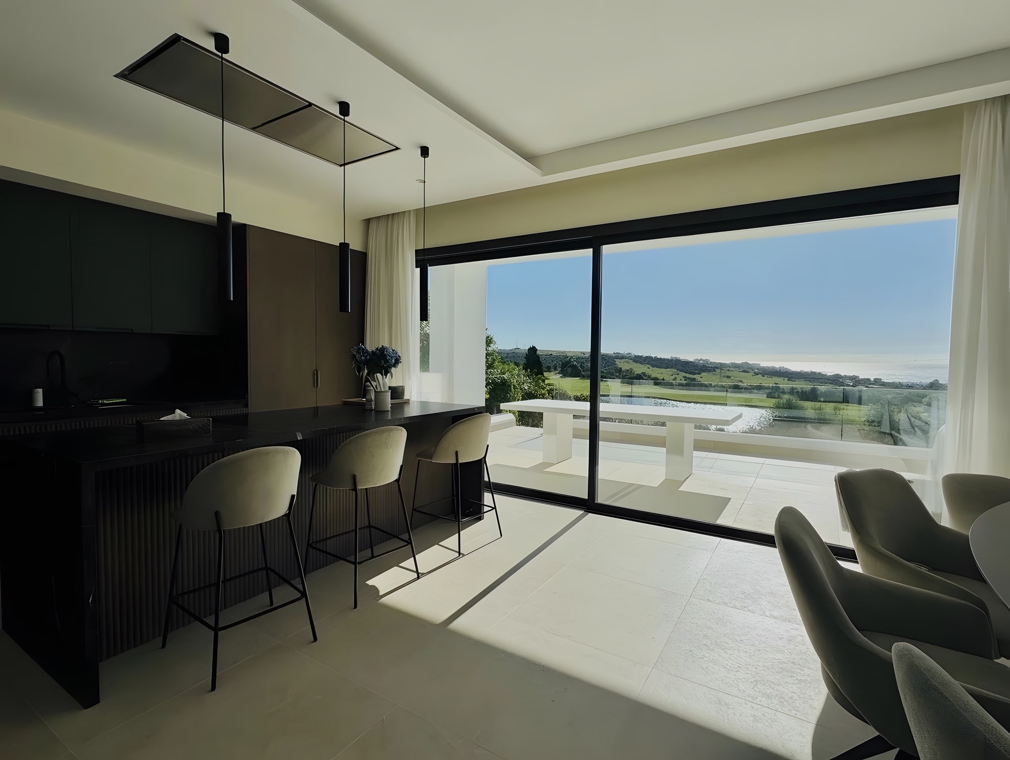 Open-plan kitchen and dining area with panoramic glazing and long views across Estepona
