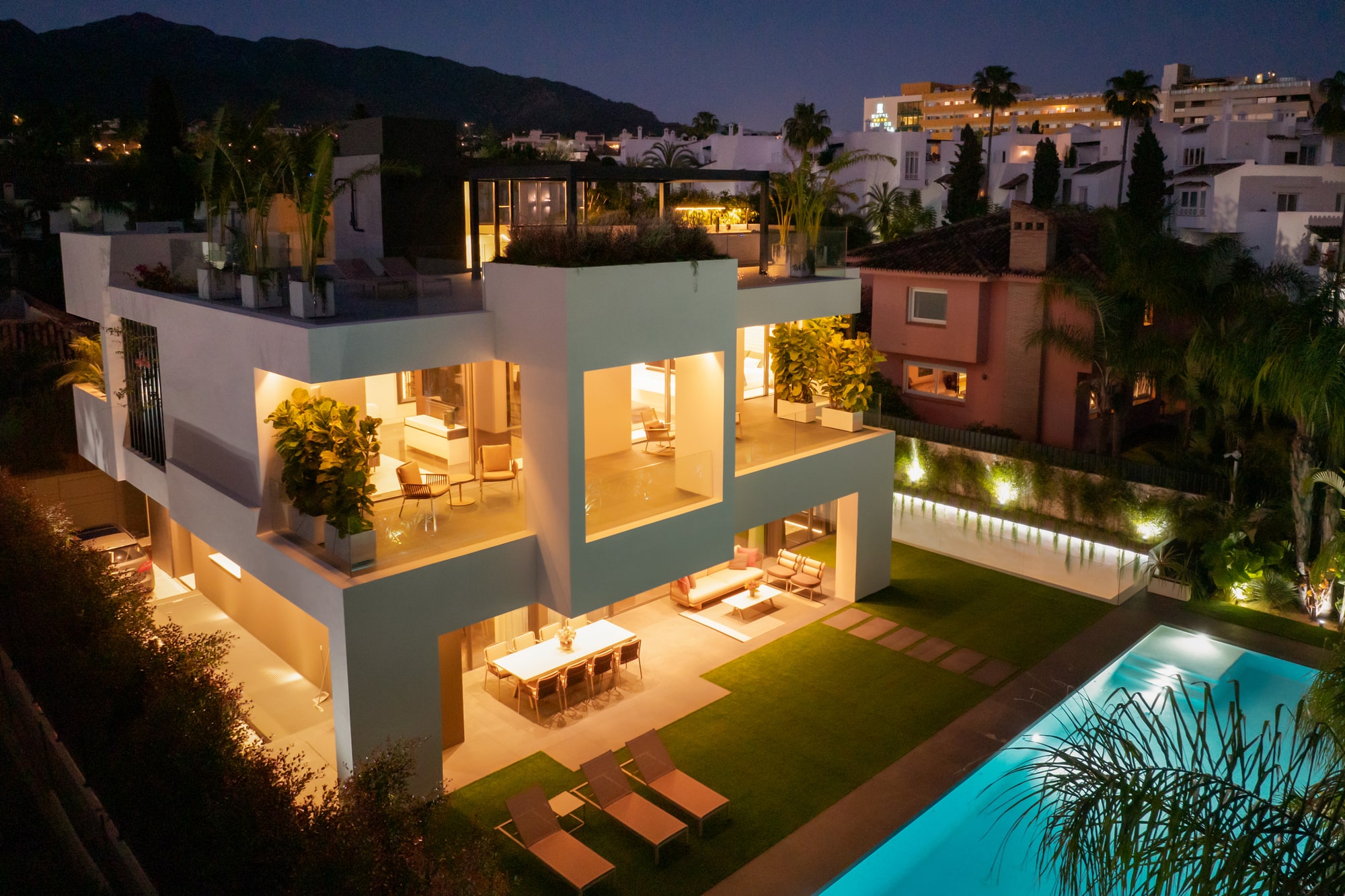 Night-time garden façade of Casa Velázquez with warm interior glow, outdoor lounge and illuminated pool composition