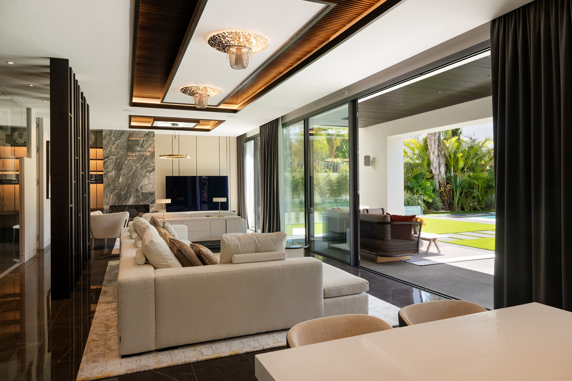 Living area framed by dark joinery and floor-to-ceiling glazing at Casa Velázquez, opening visually to landscaped exteriors