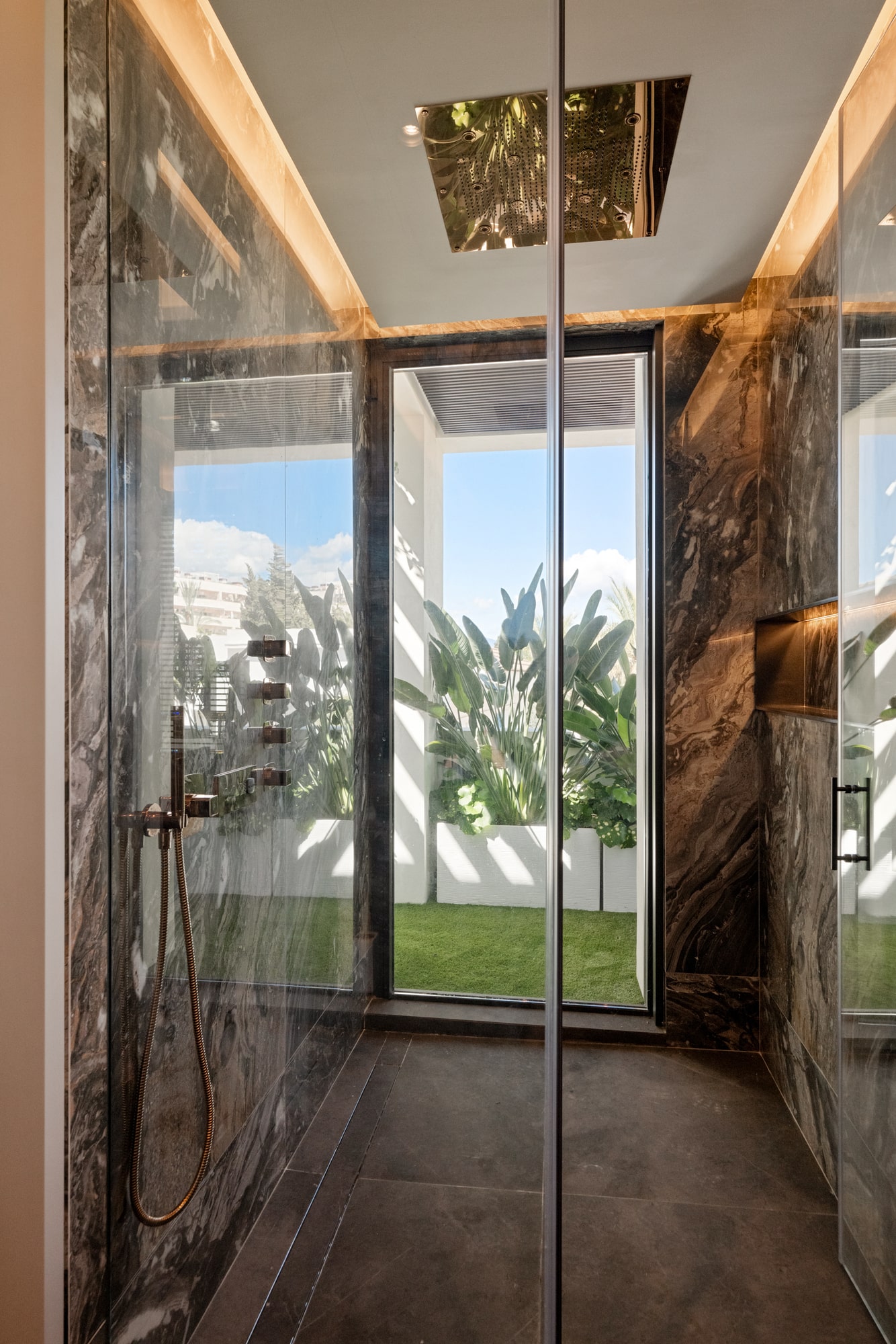 Shower space at Casa Velázquez with marble enclosure, framed garden view and spa-like residential character