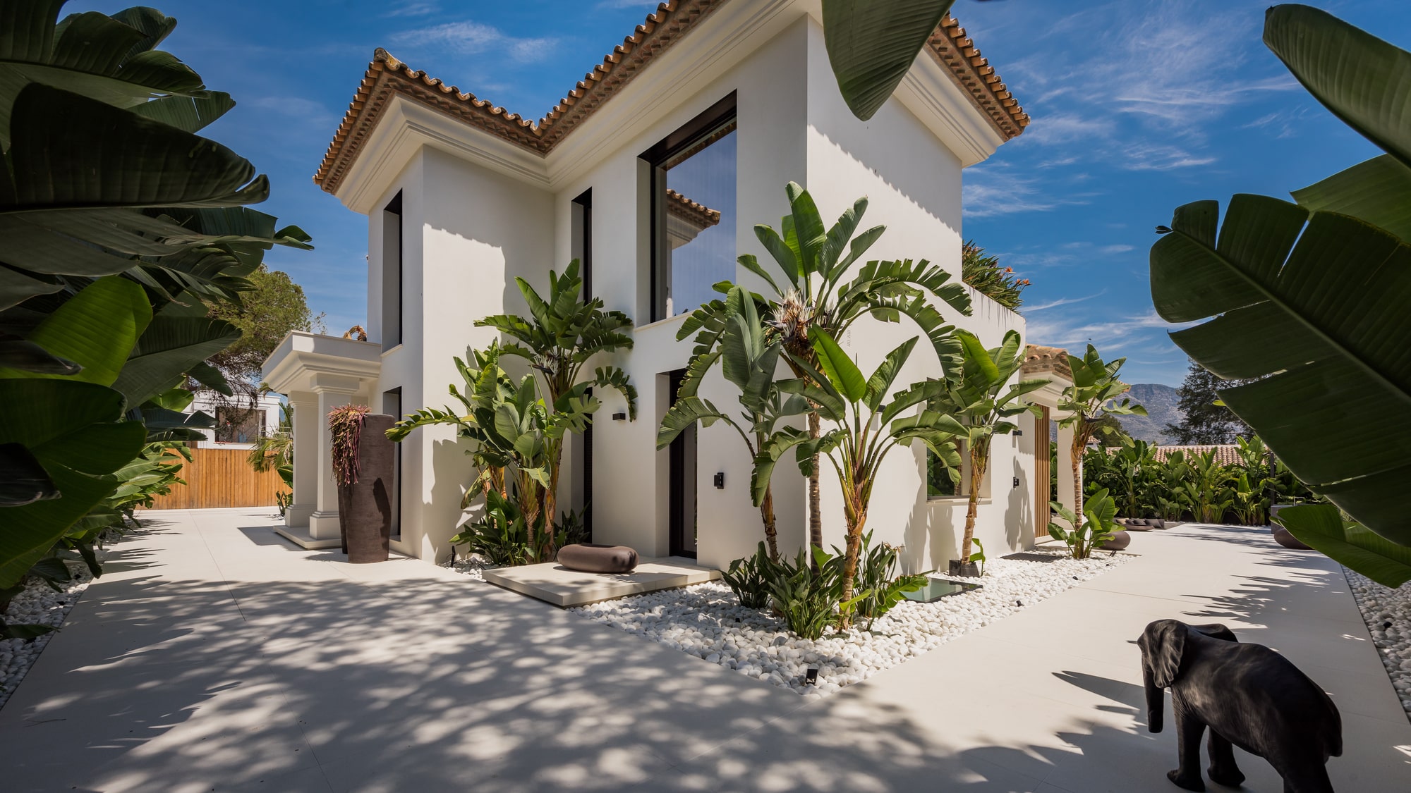 Main entrance courtyard at Villa Zarina framed by tropical planting, natural textures and crisp Mediterranean architecture